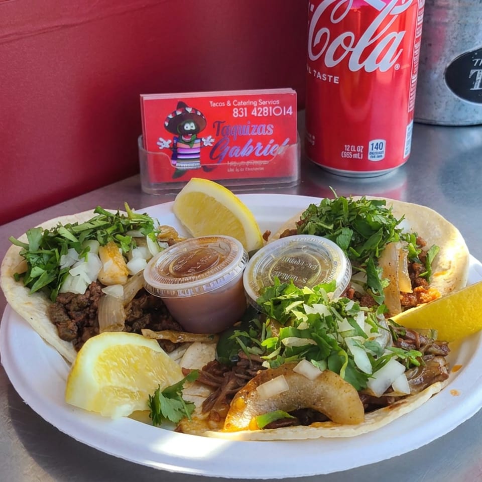 Plate of Mexican tacos topped with cilantro and onions, served with lemon wedges and salsa cups beside a Coca-Cola.